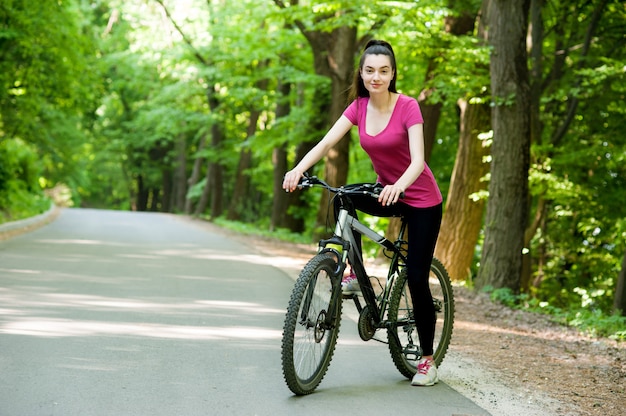 Ciclista femenina en una bicicleta en la carretera de asfalto en el bosque