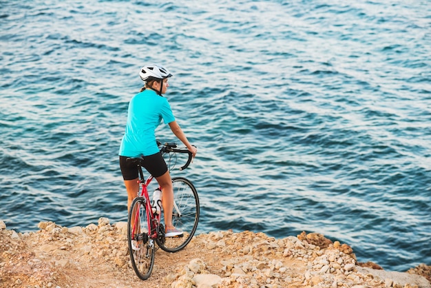 Ciclista femenina de pie en una colina y mirando al mar