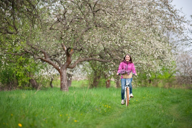 Ciclista feminina, montando uma bicicleta branca vintage no jardim primavera