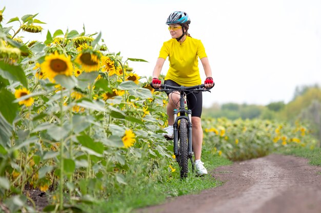 Ciclista hermosa mujer monta un campo con girasoles en bicicleta. Estilo de vida saludable y deporte. Ocio y aficiones