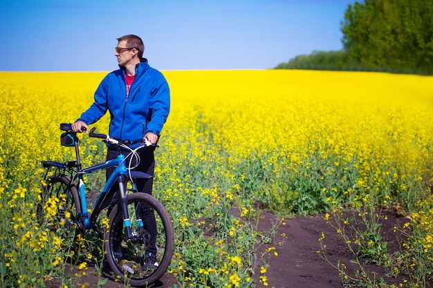 Ciclista joven paseos en campo de colza de primavera en bicicleta de montaña