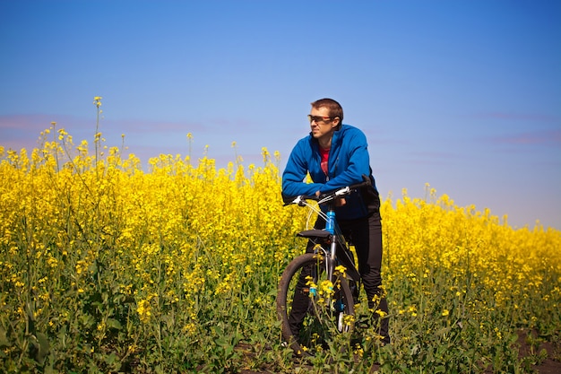 Ciclista joven paseos en campo de colza de primavera en bicicleta de montaña