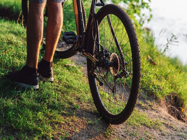 Ciclista junto a la bicicleta en el bosque verde de verano al atardecer cerca