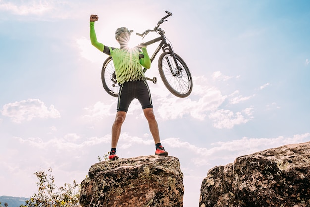 Foto ciclista latino emocionado carregando sua bicicleta acima da cabeça após terminar de pedalar na montanha