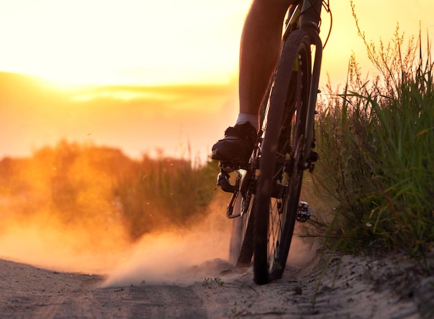 El ciclista levanta una gran cantidad de polvo de la rueda trasera en un camino de arena en un campo al atardecer