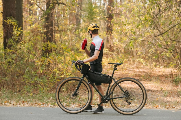 Ciclista masculina andando no parque outono com garrafa de água na mão e olhando para longe