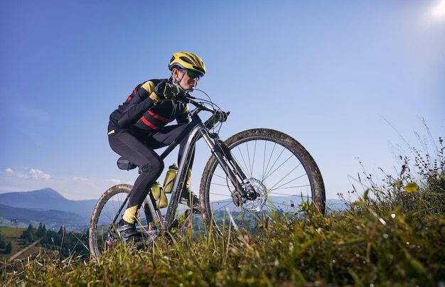 Ciclista masculino alegre montando bicicleta cuesta arriba bajo un cielo azul