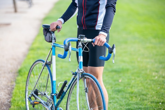 Ciclista masculino en forma joven irreconocible en ropa deportiva sentado en bicicleta en el parque