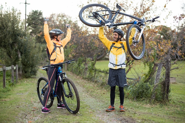 Ciclista masculino llevando bicicleta de montaña mientras ciclista femenino animándolo