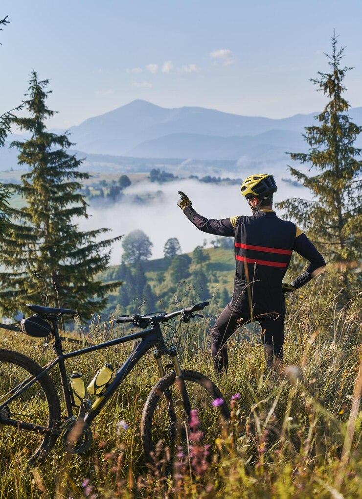 Ciclista masculino señalando con el dedo a las hermosas montañas nubladas