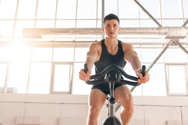 Ciclista masculino treina em bicicleta ergométrica em sala iluminada cara em roupas esportivas senta-se no simulador