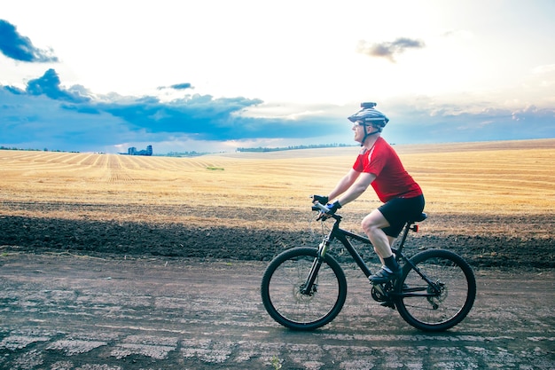 Ciclista monta una bicicleta en la carretera cerca del campo. Deportes al aire libre. Estilo de vida saludable.