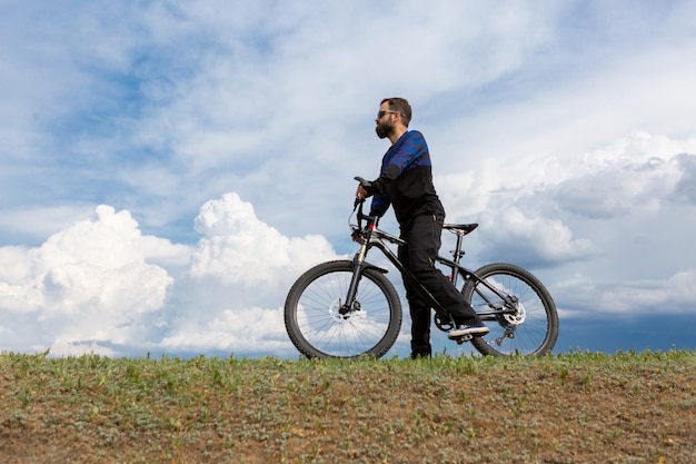 Ciclista de montaña barbudo monta montañas contra el hermoso cielo