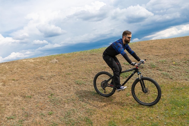 Ciclista de montaña barbudo monta montañas contra el hermoso cielo