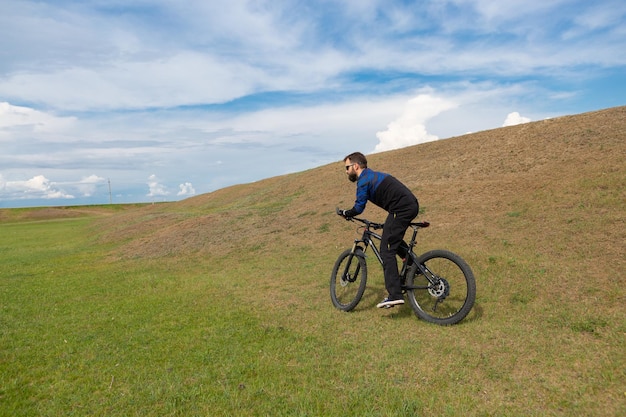 Ciclista de montaña barbudo monta montañas contra el hermoso cielo