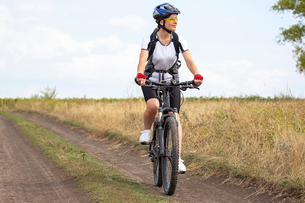 Ciclista mujer hermosa y feliz monta una bicicleta en la carretera en la naturaleza. Estilo de vida saludable y deportes. Ocio y aficiones