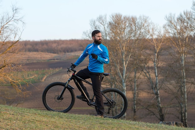 Ciclista con pantalones y chaqueta de lana en una moderna bicicleta rígida de carbono con horquilla de suspensión neumática El tipo en la cima de la colina anda en bicicleta