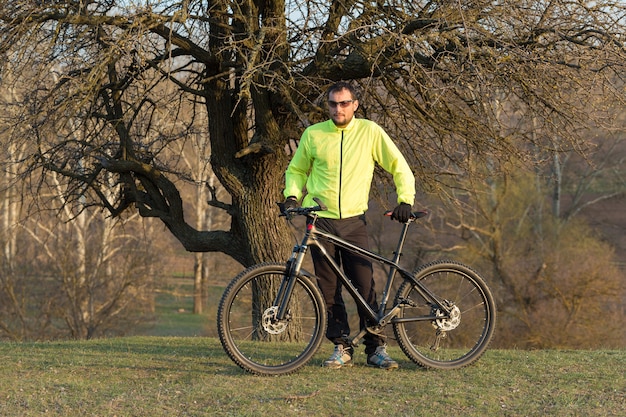 Ciclista en pantalones y chaqueta verde en una moderna bicicleta rígida de carbono con una horquilla de suspensión neumática. El chico de la cima de la colina anda en bicicleta.