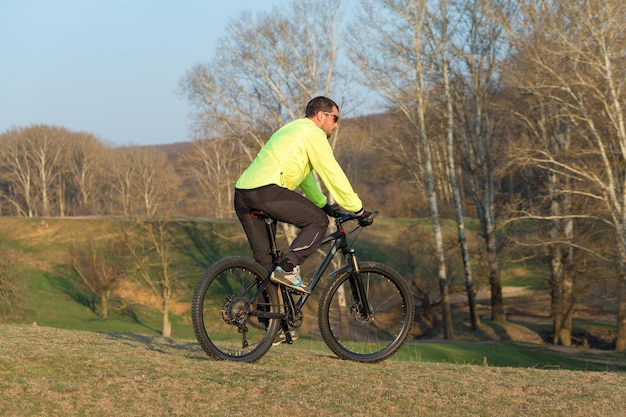 Ciclista con pantalones y chaqueta verde en una moderna bicicleta rígida de carbono con horquilla de suspensión neumática El tipo en la cima de la colina monta una bicicleta