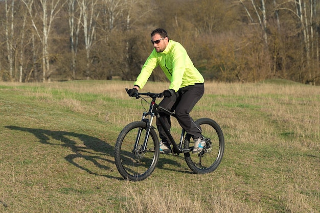 Ciclista con pantalones chaqueta verde en una moderna bicicleta rígida de carbono con horquilla de suspensión neumática el tipo en la cima de la colina monta una bicicleta | Foto