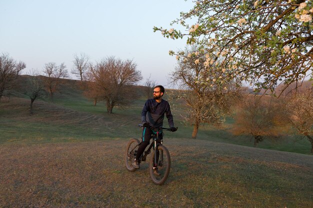 Ciclista en pantalones cortos y jersey en una moderna bicicleta rígida de carbono con una horquilla de suspensión neumática de pie sobre un acantilado con el telón de fondo de un bosque de primavera verde fresco