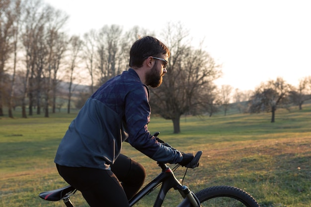 Ciclista en pantalones cortos y jersey en una moderna bicicleta rígida de carbono con una horquilla de suspensión neumática de pie sobre un acantilado con el telón de fondo de un bosque de primavera verde fresco