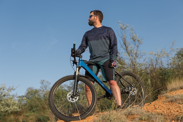 Ciclista en pantalones cortos y maillot en una moderna bicicleta rígida de carbono con una horquilla de suspensión neumática