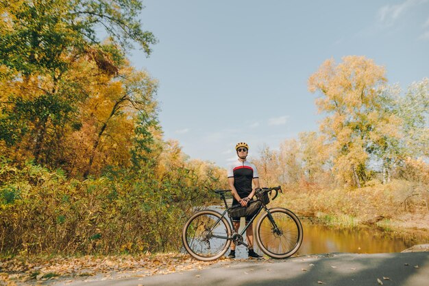 ciclista de pie con bicicleta en el fondo del hermoso paisaje otoñal y mirando a la cámara