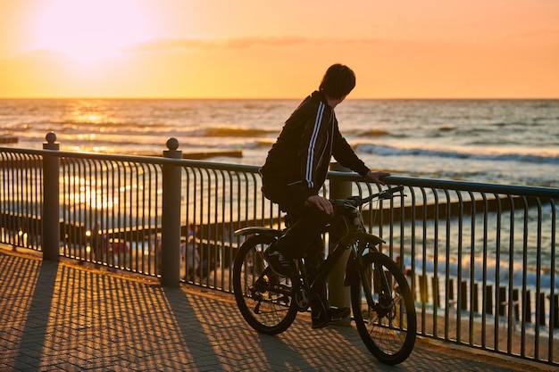 Ciclista de pie y mirando la hermosa puesta de sol sobre el mar azul deporte en bicicleta en la costa del mar Hombres ciclistas en épica puesta de sol amarilla sobre el mar deporte de bicicleta de verano