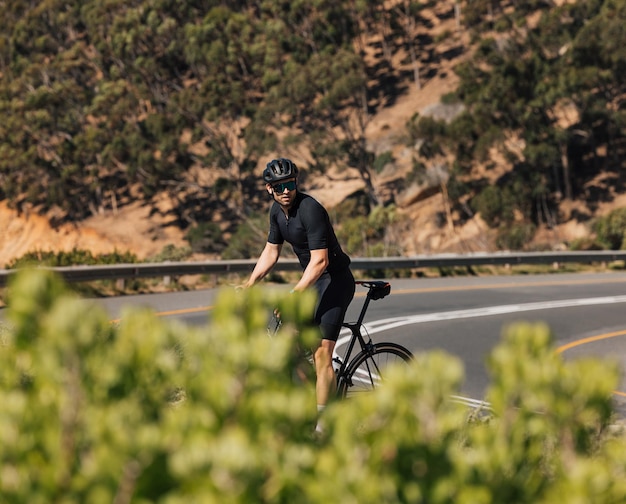 Foto ciclista profesional en ropa deportiva negra tomando un descanso en la carretera durante el entrenamiento