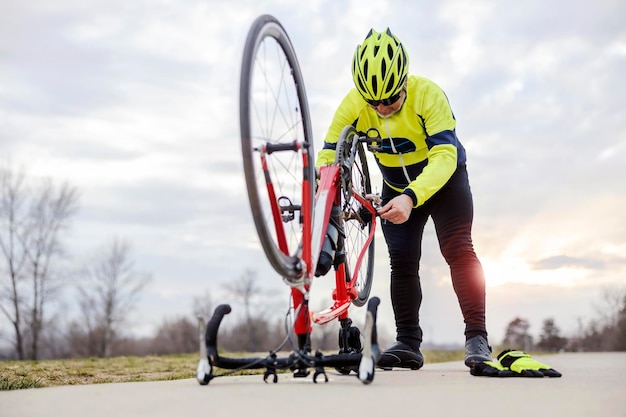 Un ciclista senior arreglando una bicicleta en la naturaleza