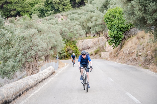 Ciclista sênior com dois ciclistas irreconhecíveis ao fundo em uma passagem na montanha