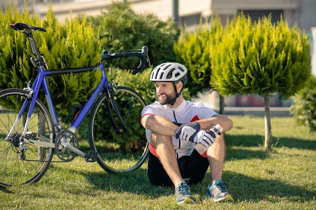 Ciclista sentado en el césped cerca de la bicicleta