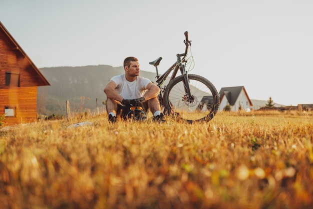 El ciclista se sienta en un prado mientras descansa de un extenuante paseo por caminos de montaña El ciclista se enfría con agua Enfoque selectivo Foto de alta calidad