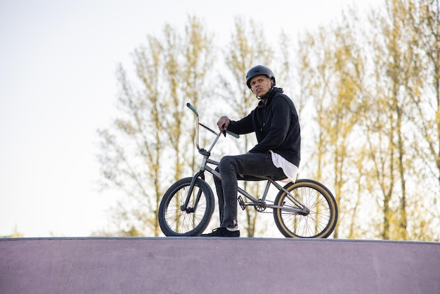 El ciclista se sienta en su bicicleta humilde un bmx en zapatillas y ropa suelta con un casco en la cabeza