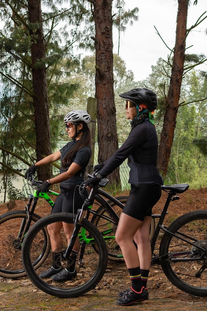 Ciclistas femininas em pé segurando suas bicicletas no meio da floresta Foco seletivo