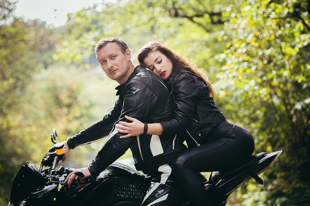 ciclistas en ropa de cuero, hombre y mujer, sentado en una motocicleta deportiva negra en el bosque