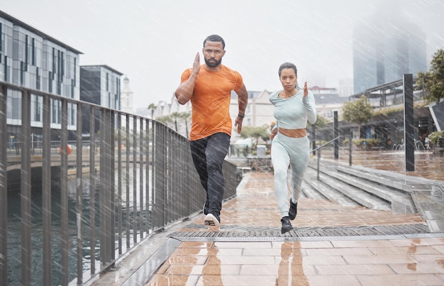 Cidade de fitness e casal na chuva correndo para treinamento de maratona de treino e exercício no inverno Bem-estar esportivo e homem e mulher correm para desafio de resistência e desempenho corporal na cidade urbana