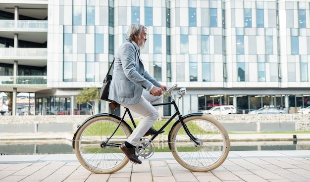 Cidade de viagem e empresário asiático em bicicleta para trabalhar na cidade urbana para baixa pegada de carbono Transporte de sustentabilidade e homem sênior andando de bicicleta para o local de trabalho para um trajeto ecológico