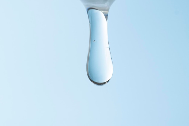 Ácido hialurónico que fluye en un chorro sobre un primer plano de fondo azul Macro de producto líquido transparente cosmético