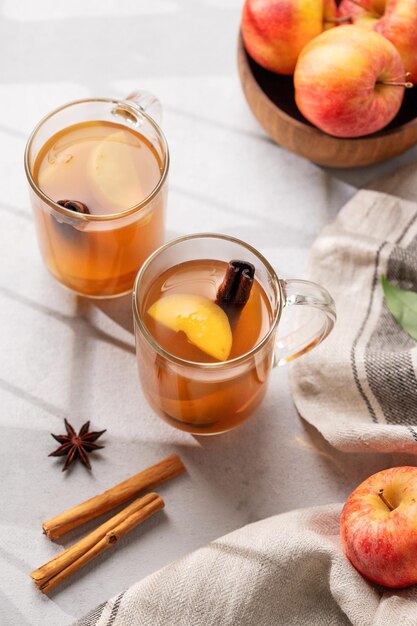 Foto cidra de maçã caseira com maçãs e canela em copos em um fundo claro com frutas frescas, especiarias e sombras o conceito de uma bebida saudável de outono ou inverno