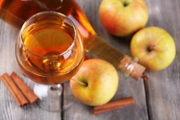 Cidra de maçã em copo de vinho e garrafa com paus de canela e maçãs frescas em fundo de madeira