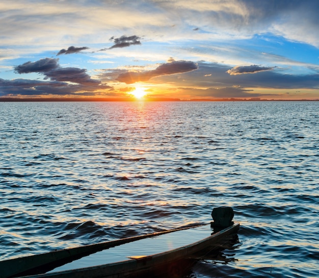 Cielo del atardecer y viejo barco pesquero de madera ahogado en la orilla del lago de verano.