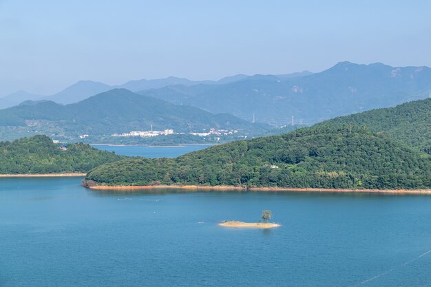 Foto cielo azul, montañas verdes y árboles rodean el lago.