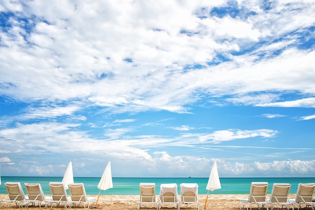 Cielo azul con nubes blancas y playa con hamacas y sombrillas sobre fondo natural en Miami, Estados Unidos. Vacaciones de verano en el paraíso. Concepto de tomar el sol y nadar. Recreación, relax y lounge