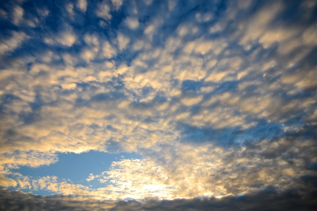 El cielo azul con nubes esponjosas doradas y sol.