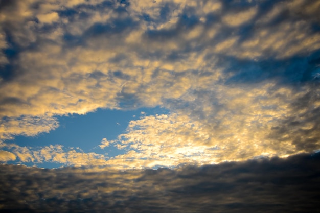 El cielo azul con nubes esponjosas doradas y sol.