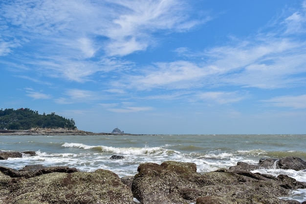 Bajo el cielo azul, las olas golpean las rocas en la playa.