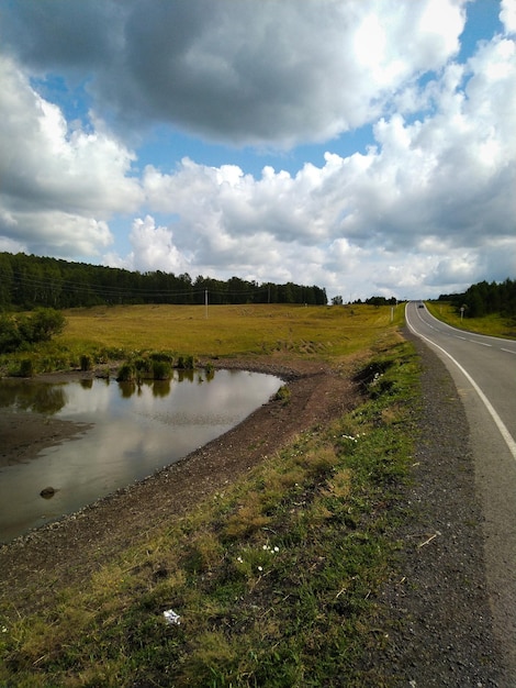 Cielo de estanque de árboles de carretera con nubes y pradera