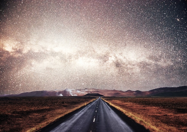 Cielo estrellado sobre las montañas. La carretera de asfalto con marcas blancas.